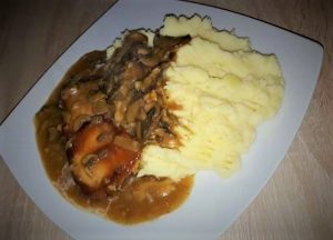 A plate with mashed potatoes and meat, topped with onion and red wine gravy.