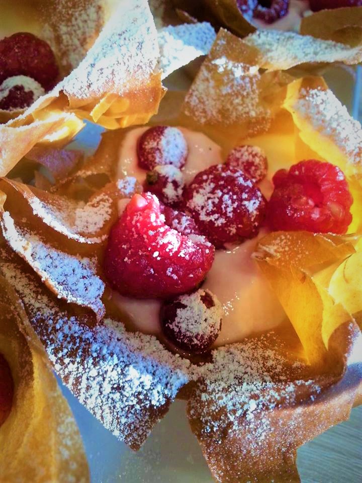 A plate of pastries with raspberries and powdered sugar.