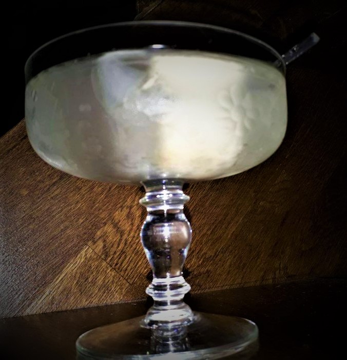 A Lychee Martini with a straw sitting on top of a wooden table.