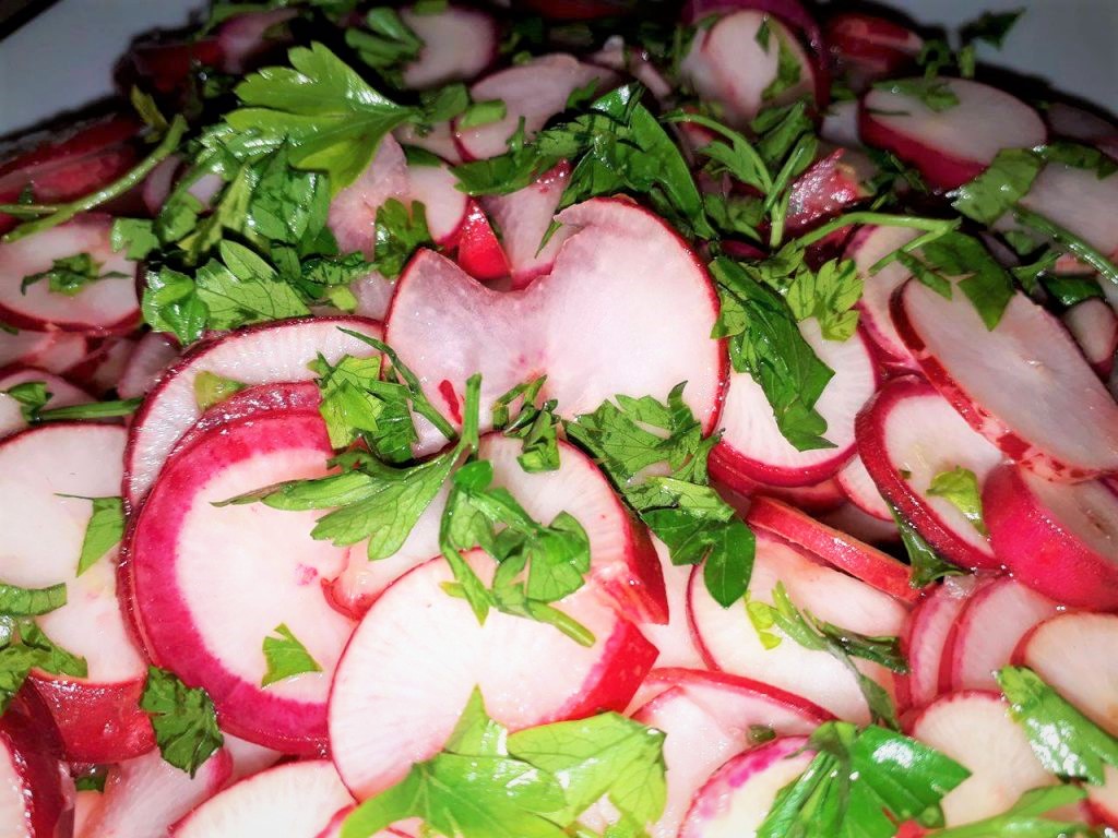 Sliced red radishes and parsley on a plate.