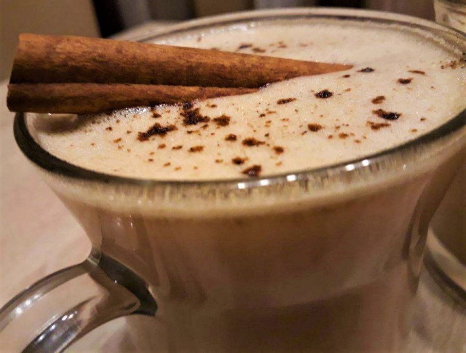A cup of hot coffee with cinnamon and cinnamon sticks.