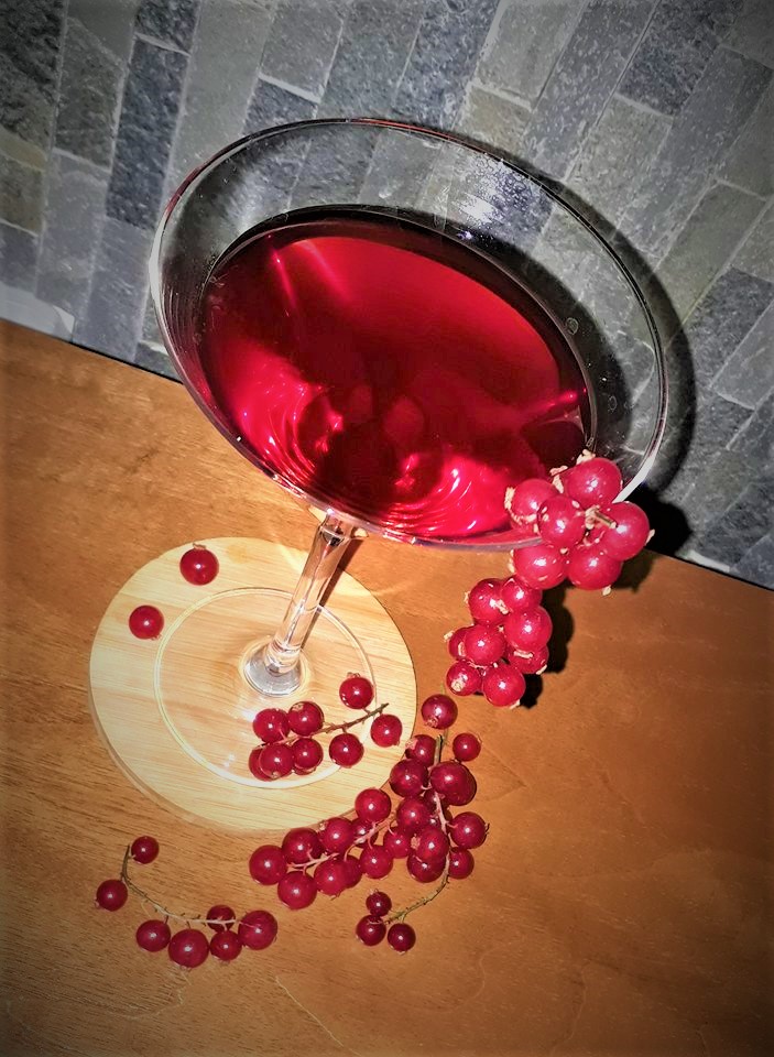 A martini with red berries on top of a wooden table.