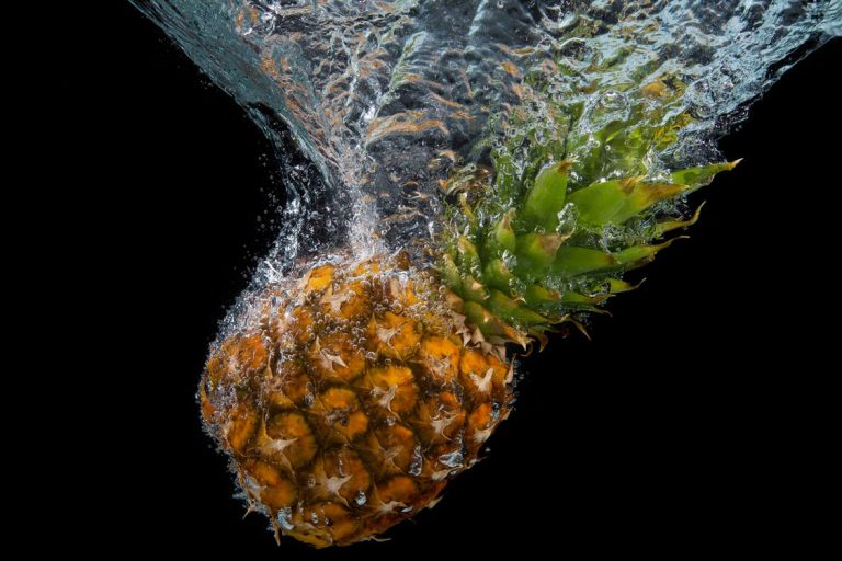 A pineapple being splashed with water on a black background.
