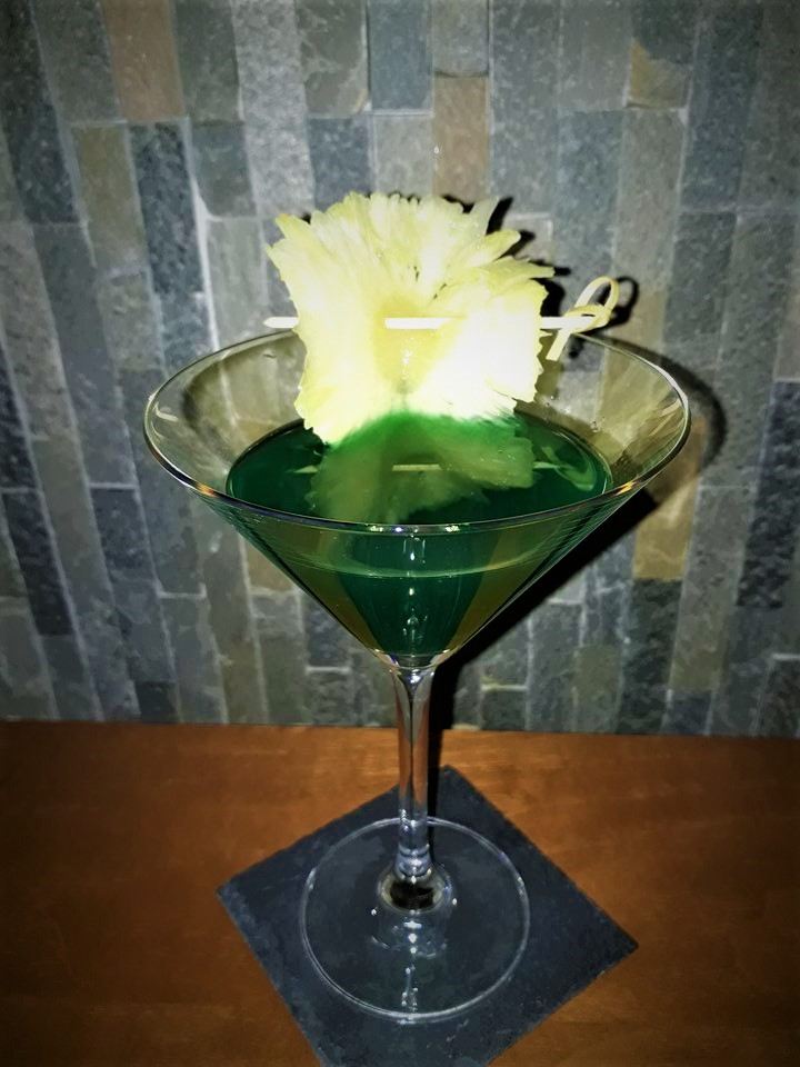 A green martini with a pineapple garnish.