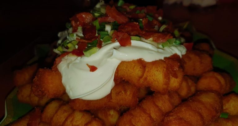 A plate of fries with bacon and sour cream.